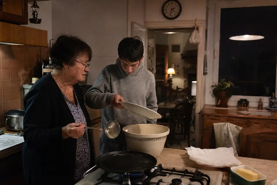 Une grand-mère et son petit-fils soulèvent l’assiette qui couvre un saladier de pâte à crêpes, pendant qu’une poêle chauffe sur la gazinière.